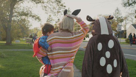 Стоковое видео: Woman with two children in carnival costumes in honor of Halloween. Walking down the street of a small American town