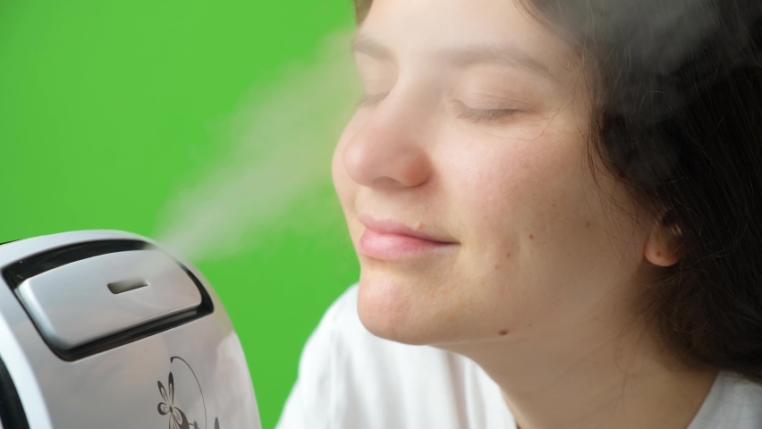 A woman enjoys pleasant moist air from a humidifier on a green screen chromakey background. | Shutterstock HD Video #1094886955