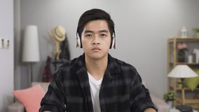 shoulder shot of a Korean man looking at camera with headset is talking and writing notes while discussing with classmate in a webinar through video call at home