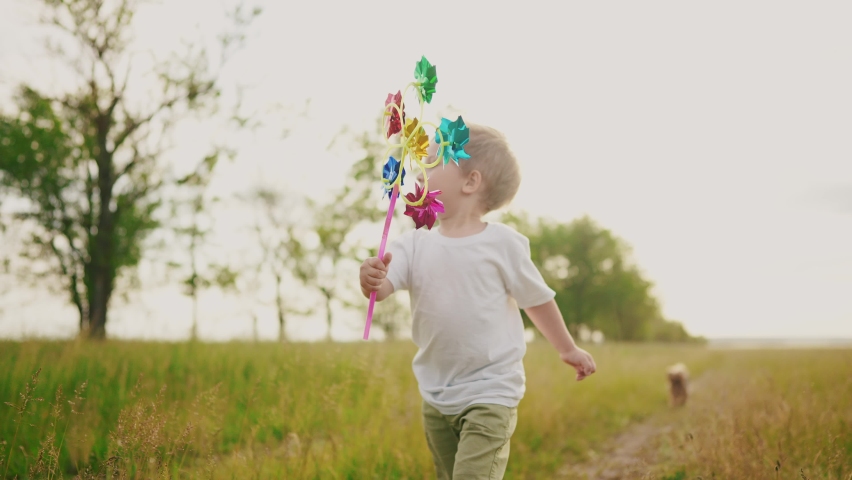 baby boy playing with spinner toy in the park. happy family kid dream concept. lifestyle baby a son plays with a toy windmill outdoors in the forest in summer
