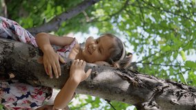 A small, beautiful girl, in a dress and headphones, sits on a tree, talking, smiling, laughing. slow motion, vertical video