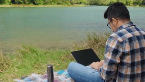 Man using laptop in nature, work remote or freelance idea, focus on working concept, studying outside, man writing on a keyboard by lake, peaceful location to study, 4k 60 fps video of park