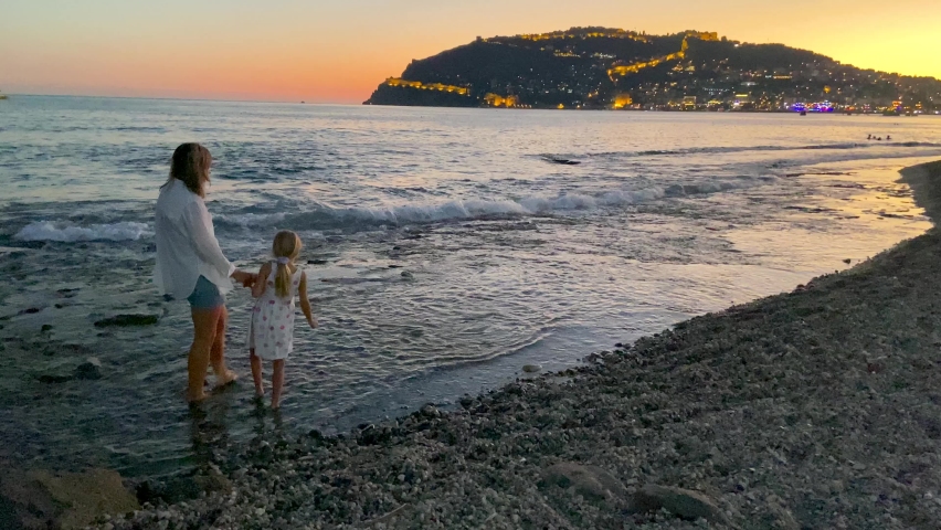 Sweet mother and daughter walk along the seashore at sunset in the summer in Turkey.
