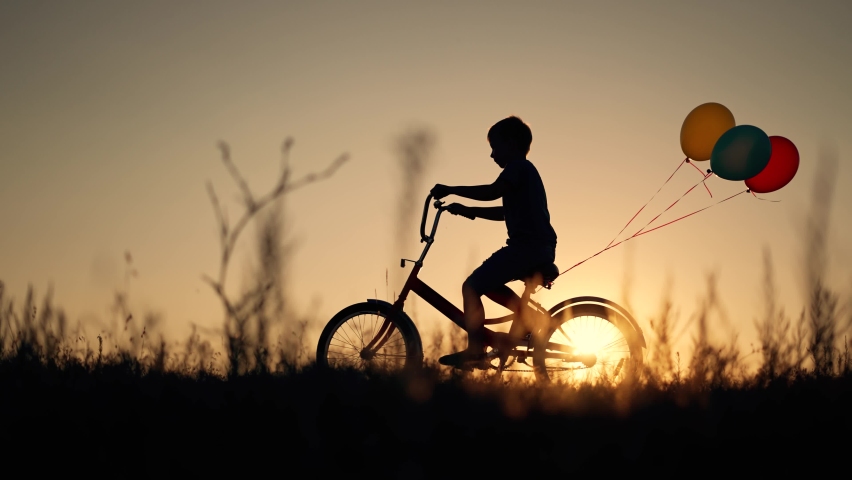 Dream child. Silhouette of child on bicycle plays in park. boy rides through natural green park with balloons. Play with balloons on bike. boy dreams of learning to ride bicycle in nature. Royalty-Free Stock Footage #1094906299