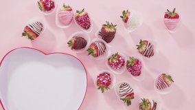 Time lapse. Flat lay. Step by step. Arranging a variety of chocolate dipped strawberries in a heart shaped gift box on pink background.