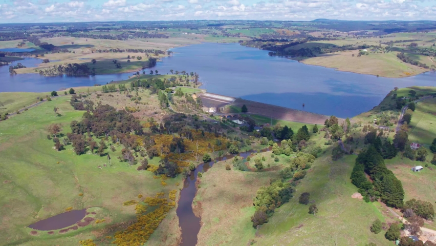 Aerial view of the Upper Coliban Reservoir dam wall, spillway and reservoir, central Victoria, Australia. September 2022. The reservoir is over 100% full and water is flowing over the spillway.