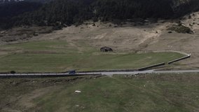 Isolated 4x4 blue car driving along solitary mountain road. Aerial sideways
