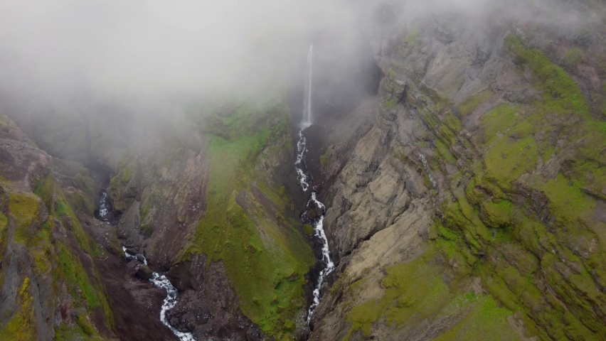 Clouds parting revealing tall waterfall and green canyon in Icelands Mulagljufur Canyon. Beautiful Scenery.