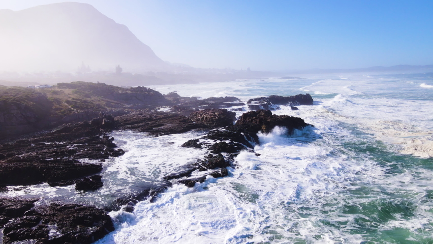 Aerial riser over rocky coastline as waves keep rolling in; Hermanus Royalty-Free Stock Footage #1094917685