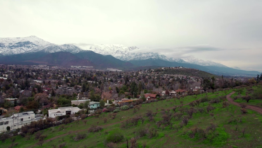Zoom in aerial view of the snow-capped Andes Mountains in Santiago, Chile. Residential houses