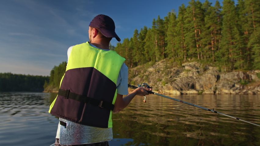 Fisherman is fishing on lake from boat using spinning rod at sunset, side view. Go Everywhere Royalty-Free Stock Footage #1094923699
