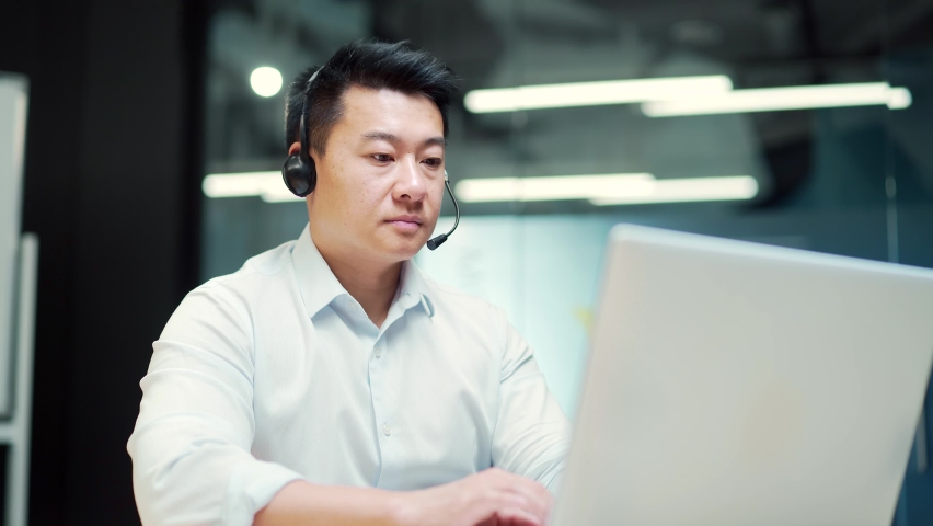 Corporate operator working in customer support service on helpline telesales. Focused man representative call center agent in wireless headset helping client with complaints using computer in office Royalty-Free Stock Footage #1094923917
