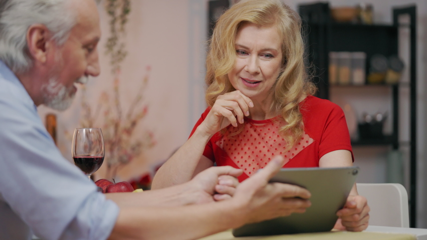 Happy middle-aged couple looking through family photos on tablet during dinner | Shutterstock HD Video #1094926151