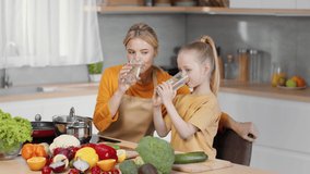 Healthy family habits. Loving mother and her little daughter drinking water together, preparing dinner and talking at kitchen, slow motion