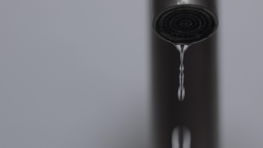 Extreme close-up of a metal water faucet on a white background isolated. Drops falling annoying in slow motion, then narrow stream flowing in slow motion 50 fps | Shutterstock HD Video #1094927483