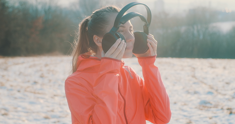 Close-up portrait Run Woman, headphone girl runner on the snow in winter sunny day. Female in pink sportswear jacket fitness training outdoors, healthy lifestyle and vitamins, 4K slow motion video