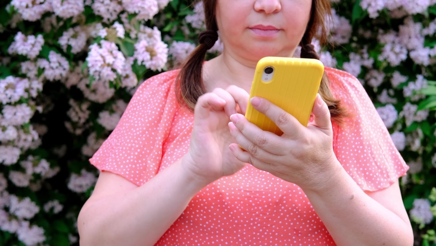 Woman years old using phone in yellow case outdoors, using phone in city, beautiful background of flowering tree, Telecommunication with friends, technology in everyday, Banking and Investment | Shutterstock HD Video #1094930557