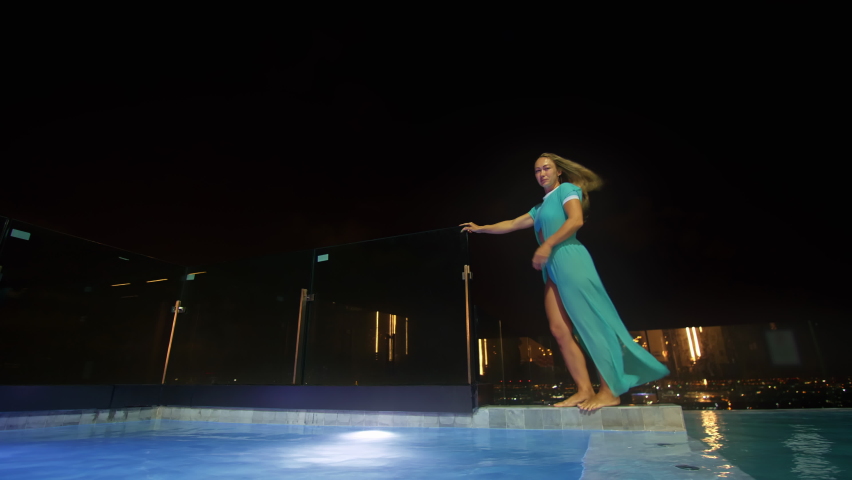 The woman tourist middle-aged alone relaxes near the pool on the roof of the hotel. The girl spends the evening in the illuminated pool hotel. Background: Night lights New York city | Shutterstock HD Video #1094931269