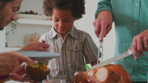 Grandfather carving turkey as multi-generation family sit around table at home and enjoy Thanksgiving meal together - shot in slow motion Video de stock