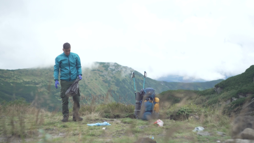 A man collects garbage and plastic in a bag in the mountains.  Royalty-Free Stock Footage #1094935395