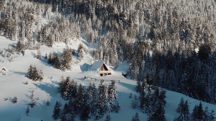 Drone shot of a small cottage house covered in snow on an icy winter morning on a sunny day. Winter fairytale in a remote forest. | Shutterstock HD Video #1094936031