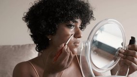 Transgender woman looking in a mirror while applying foundation with a makeup brush.
