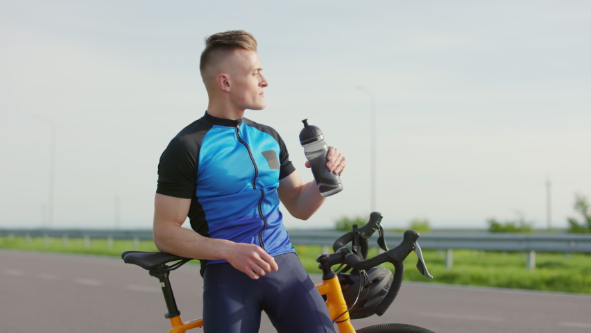 Caucasian man drinking water from bottle and taking break after riding bicycle. Active young sportsman using sport bike for exercising on fresh air. | Shutterstock HD Video #1094937089