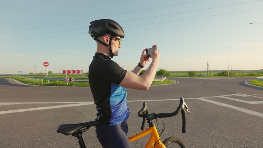 Young caucasian bicyclist in activewear using modern smartphone to take photo of incredible beautiful sunset. Concept of cycling, triathlon and modern technology. | Shutterstock HD Video #1094937091