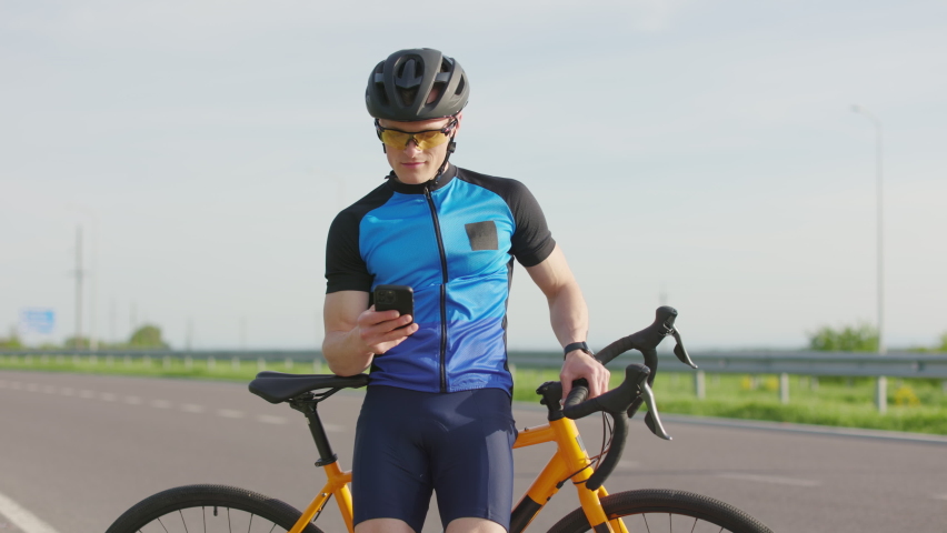 Professional cyclist in helmet and sunglasses resting while using online GPS application on mobile phone. Concept of travel, sport and modern technology. | Shutterstock HD Video #1094937093
