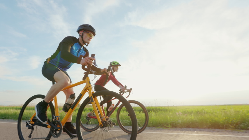 Professional racing bikers in sportswear, helmets and sunglasses riding along asphalt road with beautiful green nature around. Concept of sport and training. | Shutterstock HD Video #1094937111