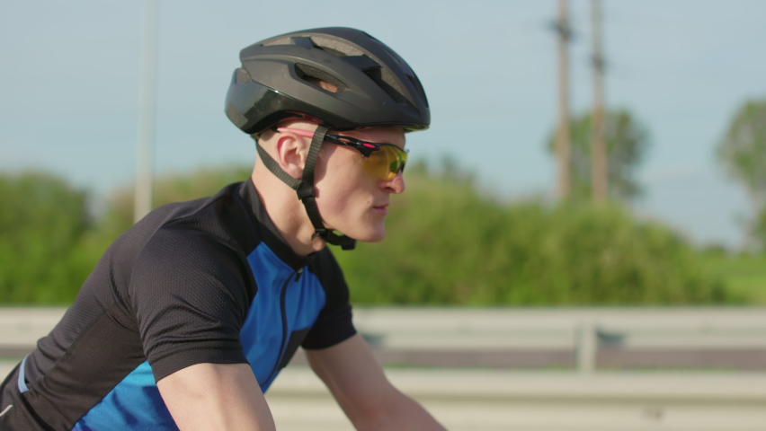 Professional cyclist wearing protective helmet and sunglasses doing workout on bicycle outdoors. Serious handsome man using road bike for outdoors training. | Shutterstock HD Video #1094937117
