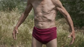 Skinny elderly man with spread hands looks in camera. Pensioner with bare torso stands in yard overgrown with wild grass against old house closeup - Powered by Shutterstock - Get 15% off with code: PIKWIZARD15