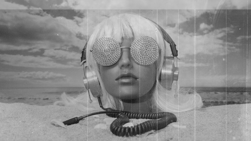 A plastic female mannequin head stuck in the sand with sparkling sunglasses and headphones on a beach | Shutterstock HD Video #1094951693