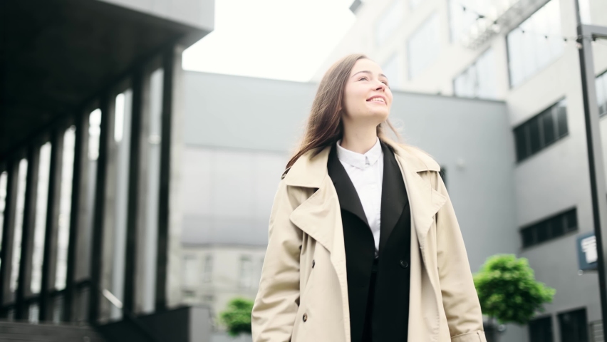 Portrait of successful young business woman in autumn look walking down near business centre. Ambitious worker smiling and looking ahead. | Shutterstock HD Video #1094954693
