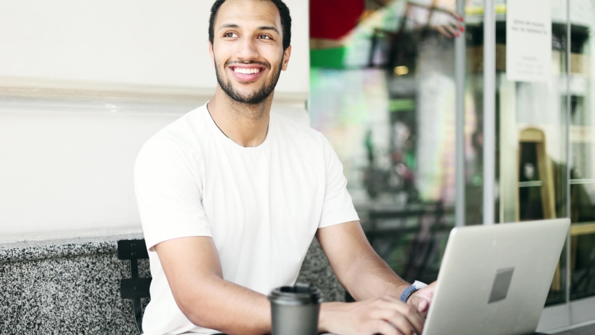 Portrait of handsome young African american man sitting in the cafe with laptop. Student learning online. Freelancer outside.  | Shutterstock HD Video #1094954695