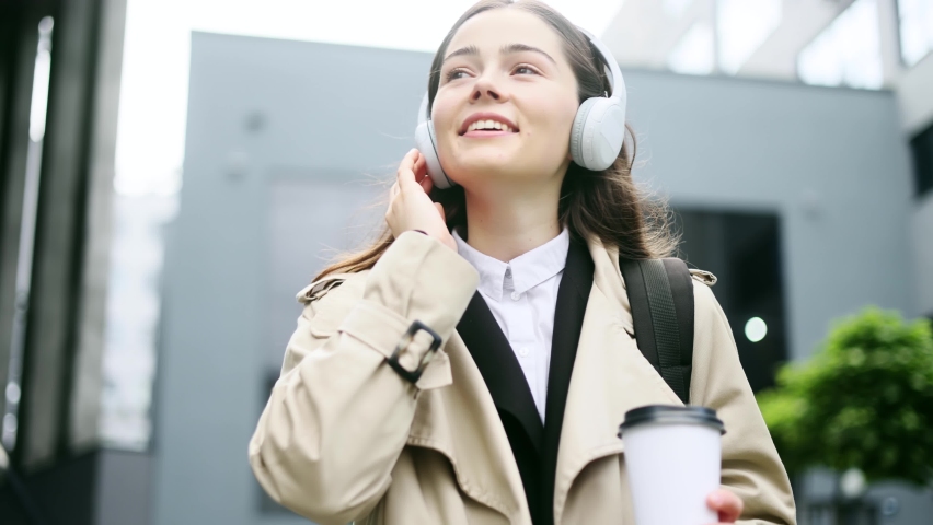 Portrait of pretty young trainee listening to music in headphones after hard work day near business centre. Young office worker listening playlist while walking down. | Shutterstock HD Video #1094954721