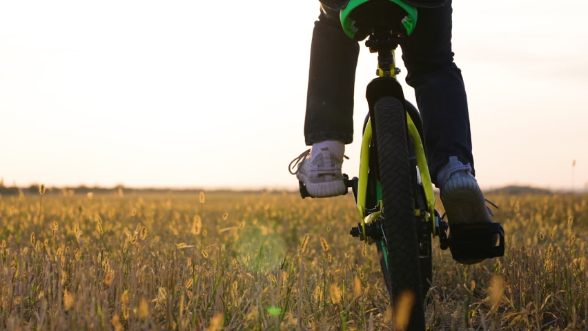 Childs feet are pedaling. Active kid, cyclist plays, rides at sunset. Little boy rides bicycle on grass field. Pedaling, bicycle wheel. Childrens travel. Physical exercise. Family in park. Free play | Shutterstock HD Video #1094955191
