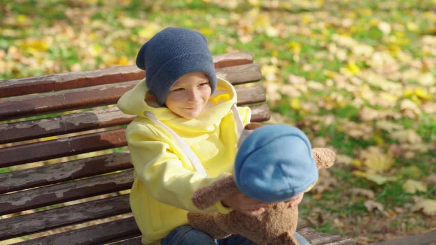Best friends plays, Child plays with teddy bear in park in autumn. Little boy hugs his favorite teddy bear on playground. Plush toy in hands of kid in autumn park. Kid is playing with toy in outdoors. | Shutterstock HD Video #1094955343