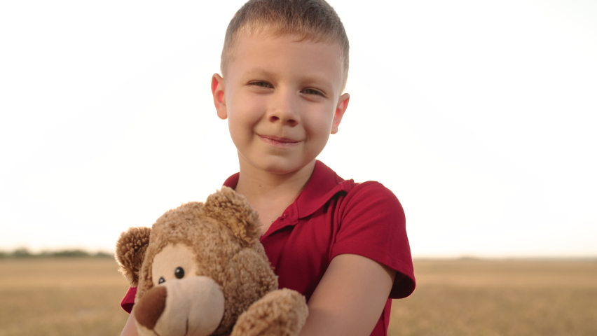 Happy little boy plays with toy bear in park against sun. Child on walk, child with teddy bear looks at camera, little kid smiles. Happy boy with friends teddy bear. Kid playing with toys in park | Shutterstock HD Video #1094955345