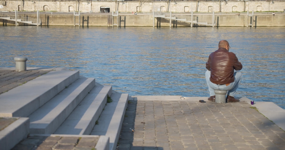 A lonely man sitting on the dock of a bay looking out to the water drinking coffee.