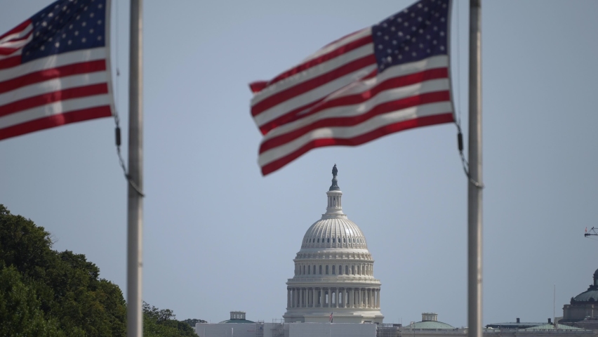US Capitol dome with flags waving at the Washington Monument in Washington DC with sunny clear blue sky on summer fall day.  Royalty-Free Stock Footage #1094958557
