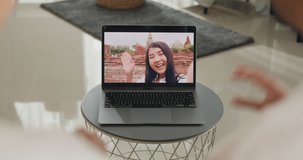 Happy young Asian couple sit on couch smiling looking at laptop screen talk video call with friends at home on holiday. Smile young husband and wife webcam conversation using internet connection.
