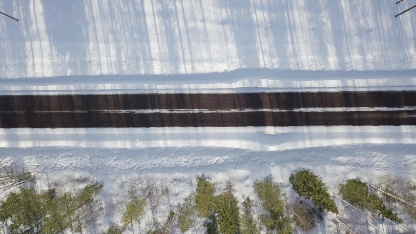 Winter icy road conditions in Finnish Lapland. Drone flying slowly left to right and camera is straight down. Black car and white van driving in same way over image area. Royalty-Free Stock Footage #1094961993