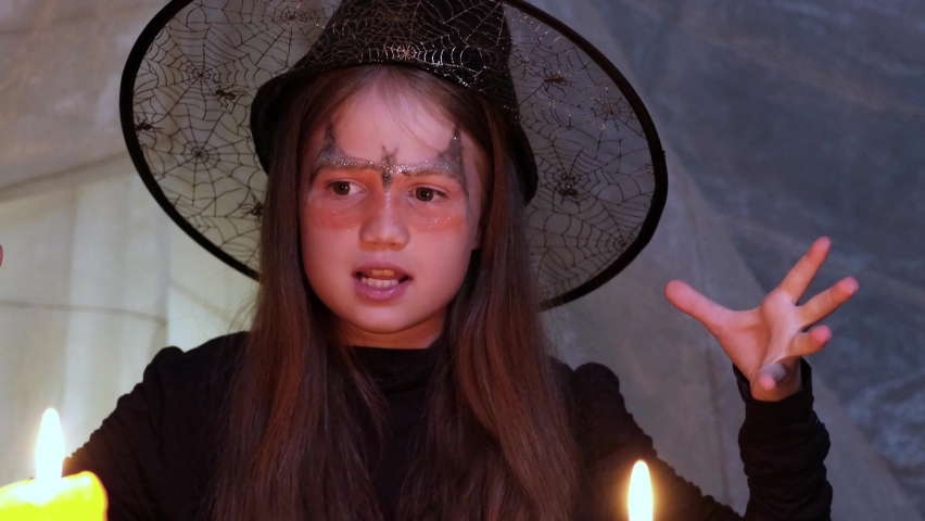 Crazy little witch reads a spell at Halloween night by candlelight. Child dressed in costume plays a witch at party indoors | Shutterstock HD Video #1094962541