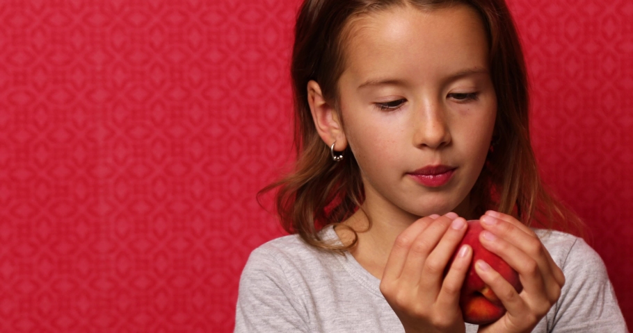 Portrait happy girl eats a peach on a red background, bites a juicy peach. The concept of enjoyment Royalty-Free Stock Footage #1094963031