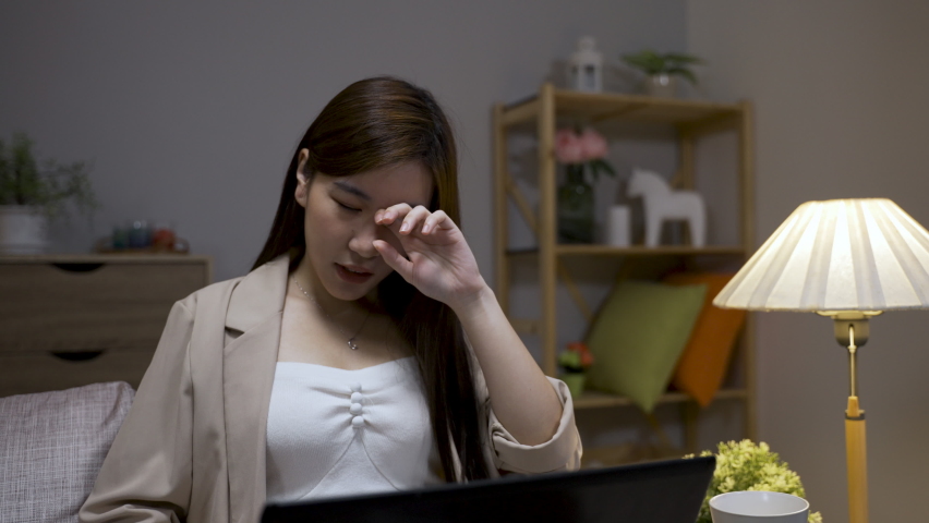overworked asian business woman is rubbing her tired eyes trying to see clearly while working overtime on the computer in the living room at home Royalty-Free Stock Footage #1094966461