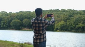 Young man takes video of forest and lake, taking video with mobile phone, enjoying in nature,  man taking a photo in forest, 4k 60 fps video of seascape, guy wandering in jungle
