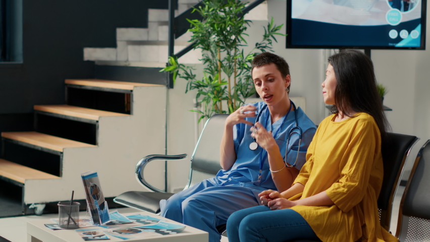 Female nurse and asian patient looking at futuristic hologram, using augmented reality and holographic image at consultation in waiting room. Analyzing high tech 3d ai at checkup. | Shutterstock HD Video #1094968431