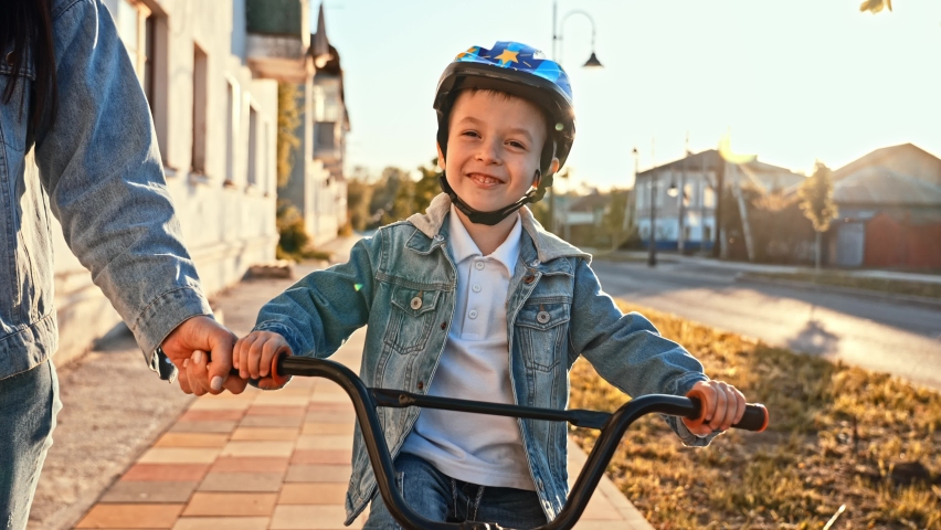 Happy smiling boy in helmet riding a cycling. Little boy learns to ride a bike in the park near the home. Sport activity for children. Child development concept. | Shutterstock HD Video #1094968845