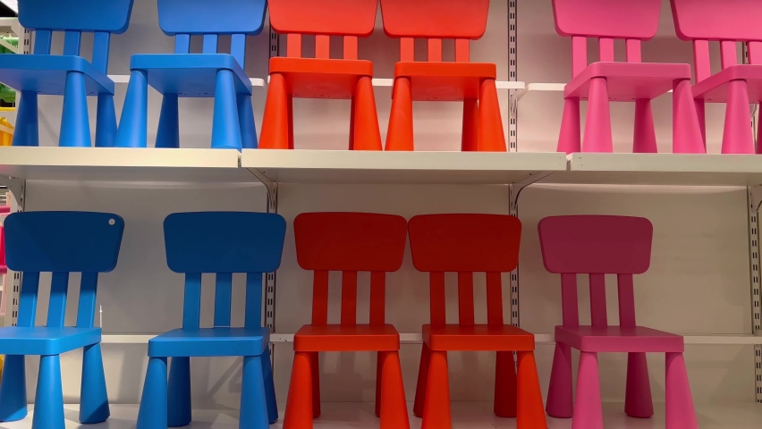 For toddlers, several little chairs in the colors red, blue, and pink are grouped together in the shelves for sale display. | Shutterstock HD Video #1094976335